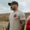 Man wearing a beige t-shirt with graphics and text, standing outdoors.