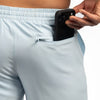 Person inserting a phone into a pocket of light blue athletic shorts.