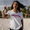 Woman wearing a white t-shirt with 'Swearing HELPS' text on a beach