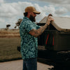 Man with tattoos and a beard adjusting a roof rack on a vehicle outdoors.