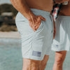 Person wearing light gray shorts with an American flag patch on a beach.