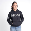 Person wearing a black hoodie with 'MOM' printed on it against a white background