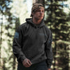 Person wearing a dark gray hoodie with logos in a forest setting