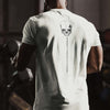Person wearing a white t-shirt with a skull design and text on the back, standing in a gym.