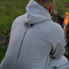 Person wearing a gray hoodie with a skull design and text on the back, sitting by a campfire.