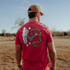 Man wearing a red t-shirt with a graphic design on the back, standing in an open field.