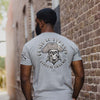 Man wearing a gray t-shirt with a skull design and text, standing against a brick wall.