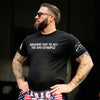 Man wearing a black t-shirt with text and American flag shorts against a dark background