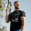 A muscular man outdoors wearing a black graphic t-shirt that reads 'STILL OPERATIONAL' with a rifle magazine illustration, holding a rifle. The t-shirt also features a white logo on the right sleeve.
