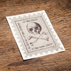 Vintage-style card with skull and crossbones design on a wooden surface