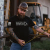 Man wearing a black t-shirt with text and tattoos, holding a tool in an industrial setting.