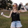 Woman in a black tank top and denim shorts holding a can and boombox outdoors.
