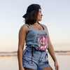 Woman wearing a tank top with a graphic design and denim shorts, standing against a blurred natural background.