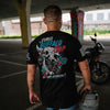A man viewed from behind wearing a black Sturgis Buffalo Chip t-shirt with a large graphic on the back, standing in an outdoor parking structure next to a motorcycle.