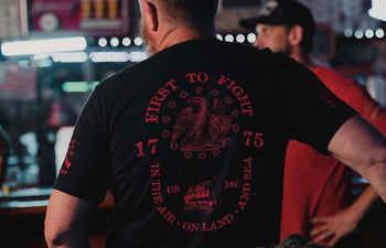 Man wearing a black t-shirt with red text and graphics in a bar setting