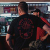 Man wearing a black t-shirt with red text and graphics in a bar setting
