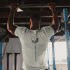 Person doing pull-ups in a gym wearing a white t-shirt with a skull design.