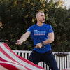 Man in blue t-shirt holding an American flag outdoors