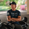 A man wearing a navy blue graphic t-shirt with 'Torque MATTERS' printed on the front, sitting on a black motorcycle in an outdoor setting.
