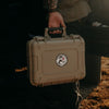 Person holding a beige hard-shell case with a logo on a dark background