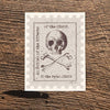 Vintage-style card with skull and crossbones design on a wooden surface