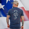 Man wearing a blue t-shirt with a snake design and text, standing in front of an American flag.