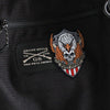 Close-up of a black fabric item featuring a large embroidered eagle skull patch with wings and a shield, alongside a smaller black rectangular patch reading 'GRUNT STYLE US GS THIS WE'LL DEFEND'.