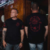 Two men wearing black t-shirts with red text and graphics, standing in a bar setting.