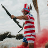 Person wearing a flag-themed outfit holding rifles with a cloudy sky background