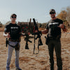 Two men holding rifles in a desert-like setting with 'Size Matters' shirts.