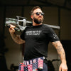 Man holding a rifle, wearing a black t-shirt with text and American flag underwear, against a dark background.