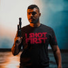 Man wearing a black t-shirt with 'I SHOT FIRST' in red, holding a space gun against a blurred background.