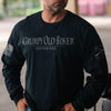 A man wearing a black long-sleeve t-shirt with 'GRUMPY OLD BIKER I RIDE WHERE I WANT' printed in white on the chest, featuring a distressed American flag on the right sleeve and a graphic on the left sleeve.