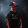 A man wearing a black graphic t-shirt with 'BUILT FOR BAD DAYS' and a firefighter helmet, posed against a dark, smoky studio background.
