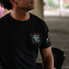 A man wearing a black short-sleeve t-shirt with a graphic of a bull skull and a star on the left chest, set against a blurred background.