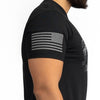 Black t-shirt with American flag design on sleeve and logo on back, worn by a person.