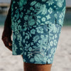 Person wearing a green and blue patterned shirt with a blurred beach background