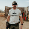 Man wearing a 'Come and Take It' t-shirt with a rifle graphic at an outdoor shooting range.