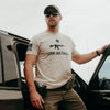 Man wearing a t-shirt with a gun graphic and text, standing next to a car.