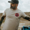 Man wearing a white t-shirt with a red logo, standing outdoors.