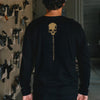 Person wearing a black long-sleeve shirt with a skull design and text on the back, standing in a workshop.