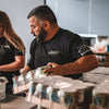 Man in a black t-shirt with visible branding working at a counter with products.