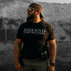 Man wearing a black t-shirt with 'DEFEND THE CHILDREN' text, standing against a textured wall.