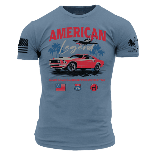 A blue short-sleeve graphic t-shirt featuring a red classic Mustang car, the words 'AMERICAN Legend' in red and white, a palm tree and airplane, and additional graphics on both sleeves.