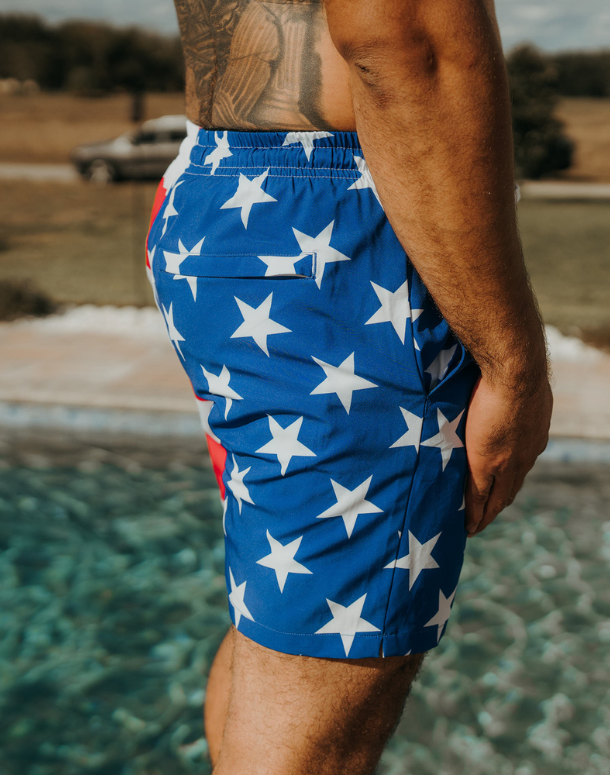 Person wearing blue swim shorts with white star pattern by a pool.