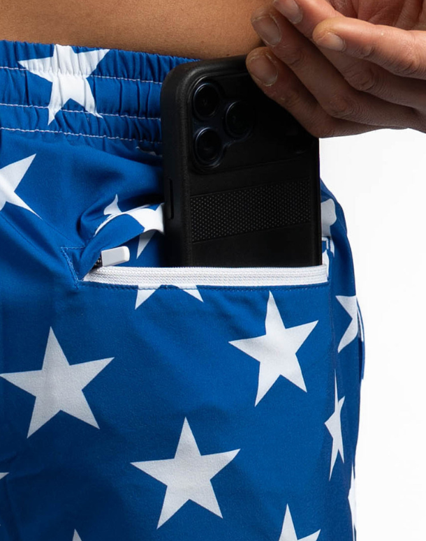 Person wearing blue shorts with white star pattern, holding a black phone case.