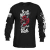 A black long-sleeve t-shirt with a graphic print on the front showing a red skull biting a knife with the text 'YOUR MOUTH IS VIOLATING MY ROE'. The right sleeve features a distressed American flag graphic, and the left sleeve has white text reading 'GIRL SHOT IN THE STFU'.