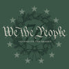 A square graphic design featuring a dark green background with a central wreath illustration in a lighter green-gray tone, decorated with pine branches, pinecones, holly leaves, and a bow. The text 'We the People' is written in large white gothic-style lettering across the wreath, with 'CELEBRATE THE SEASON' in smaller white text below.