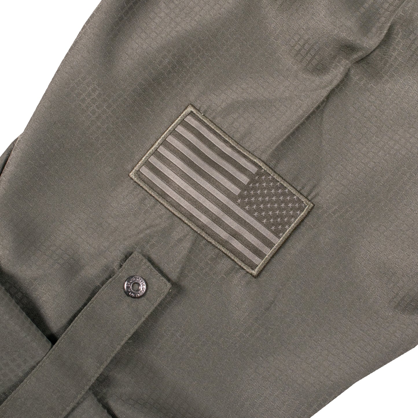 Sleeve of the Grunt Style Long Sleeve Fishing Shirt  in Olive that has the Assaulting flag logo, sleeve roll up tab, and custom buttons
