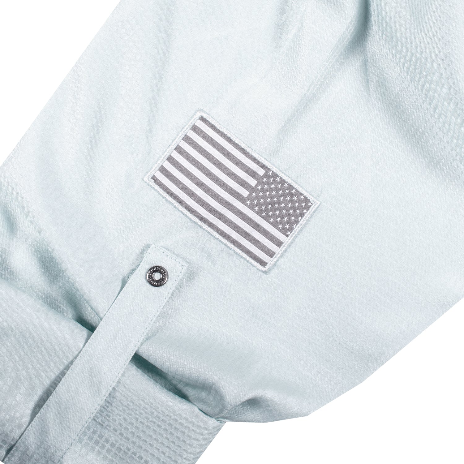The sleeve of the Grunt Style Long Sleeve Fishing Shirt in Seafoam that has the Assaulting Flag patch and sleeve roll up tabs with custom buttons